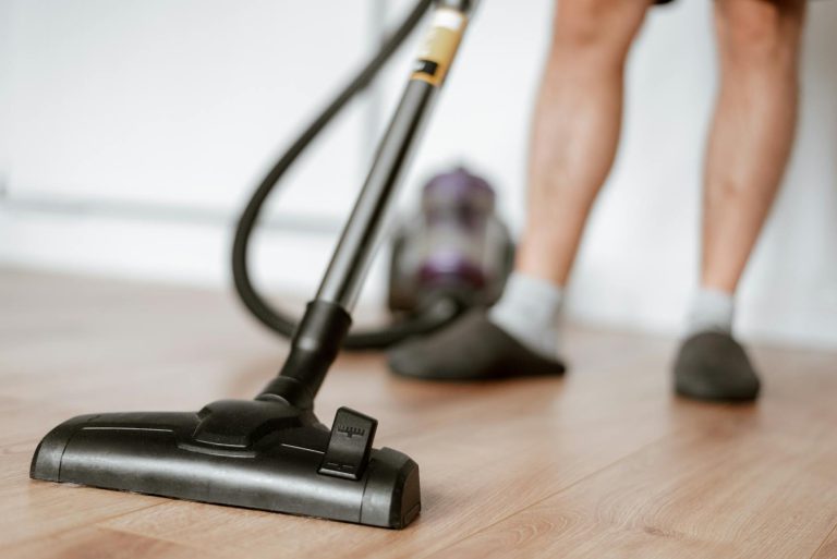A person uses a vacuum cleaner on a wooden floor for effective cleaning.